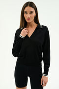 A woman poses against a plain background, wearing the SPLITS59 Taylor Knit Polo in black/white paired with black fitted shorts, her hand near the collar as she looks at the camera.