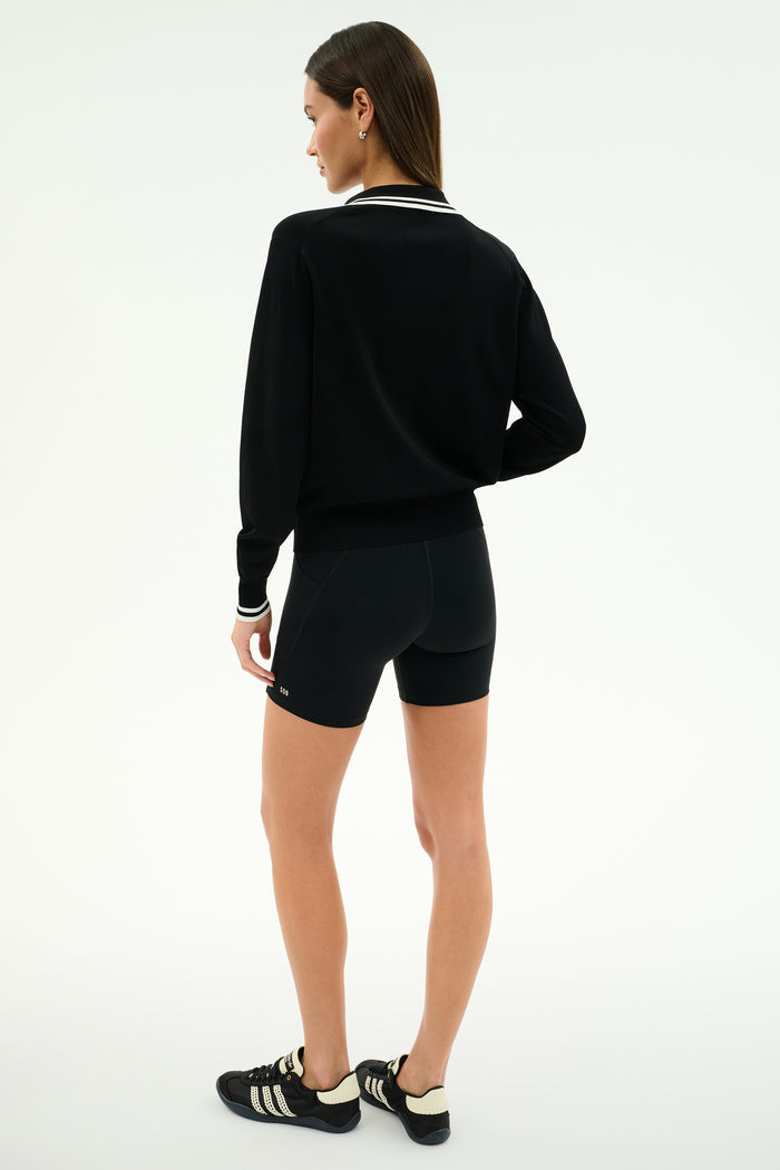 A woman stands facing away, wearing the SPLITS59 Taylor Knit Polo in Black/White against a plain white background.