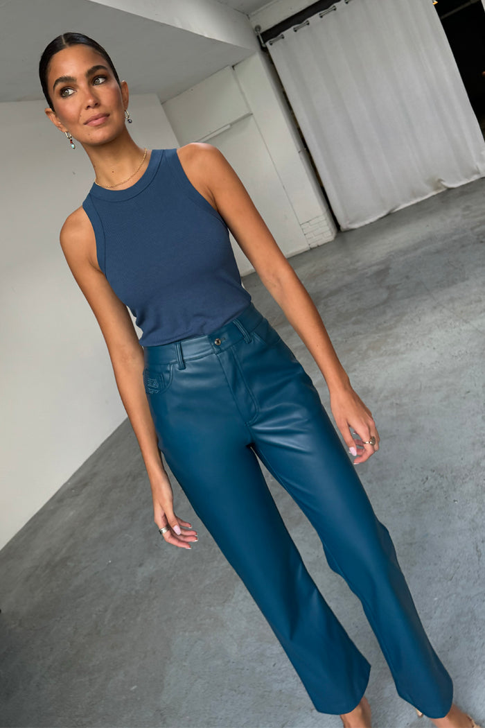 Teal straight leg vegan leather trousers and a navy ribbed tank top worn by a model.