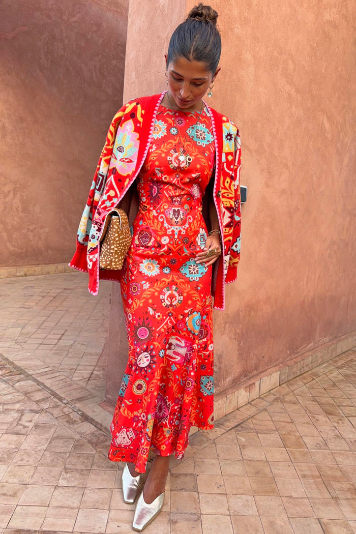 Tomato Tapestry Frida Dress in red with sun motifs, layered with a coordinating cardigan and metallic shoes.