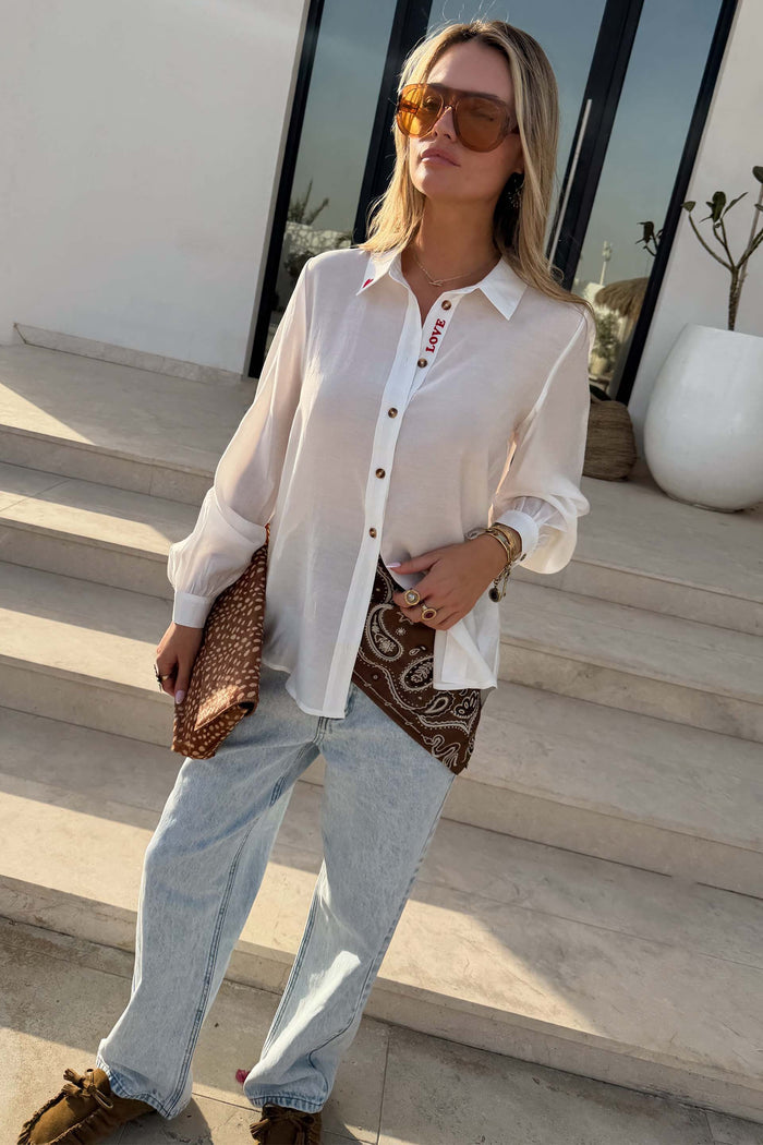 White Love Miley Shirt with tortoise buttons and red LOVE embroidery, styled with light wash denim jeans.