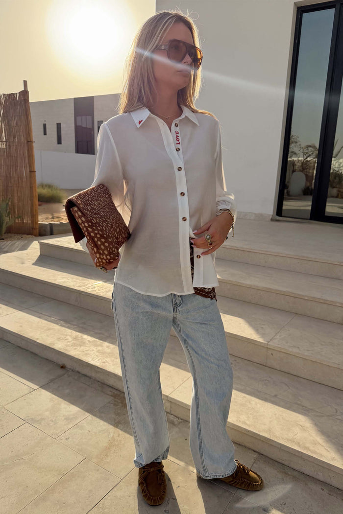 Sheer White Love Miley Shirt with heart motifs and blouson sleeves, styled with light jeans and a leopard print clutch.