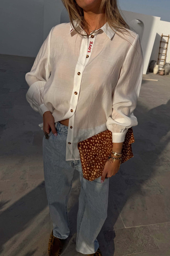 White Love Miley Shirt with sheer fabric, blouson sleeves and red LOVE embroidery, paired with jeans and a leopard clutch.