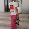 White cotton Rodeo T-Shirt with a red graphic on the back, styled with a pink paisley skirt and beaded bag.