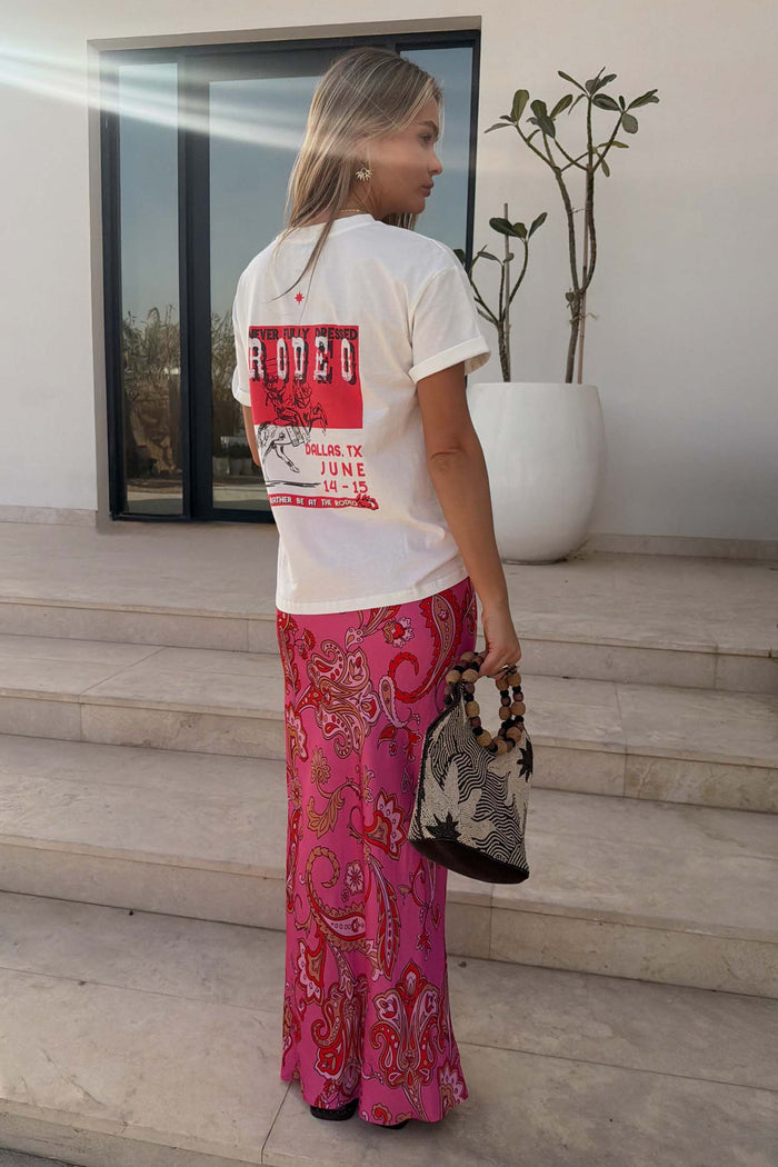 White Rodeo T-Shirt with a red graphic print on the back, styled with a pink paisley skirt and a woven bag.