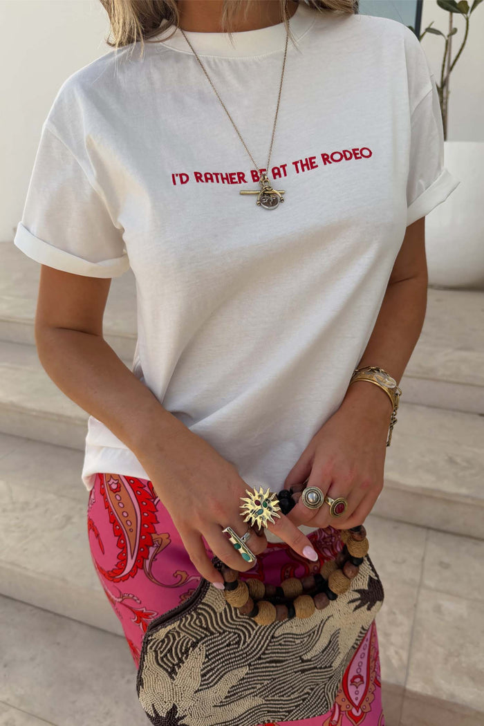 White cotton Rodeo T-Shirt with red slogan text, paired with pink patterned trousers and statement rings.