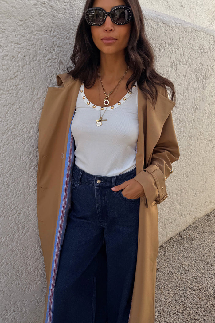 White Studded Rib Vest with gold stud detailing, styled with a camel trench coat and dark denim jeans.