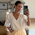 White cotton V-neck T-shirt with shoulder pads, shown in a mirror selfie styled with striped trousers.