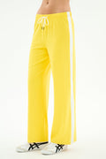 A person wears SPLITS59's Willow Airweight Wide Leg pants in bright yellow/white with white sneakers featuring black accents, standing against a white background.