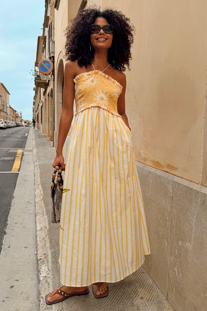 Yellow Stripe Ashley Dress with sun motifs, a frilled bandeau top and a cotton-linen striped skirt on a sunny street.