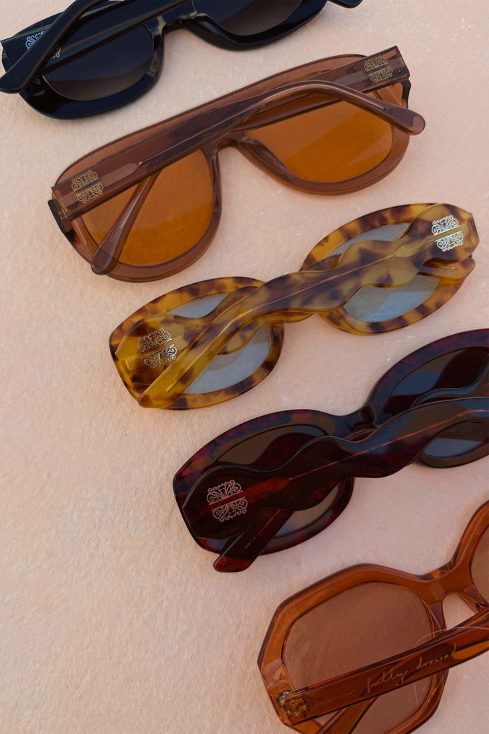 Yellow Tort Wiggle Arm Sunglasses with light blue lenses and distinctive wavy arms, shown in a row of NFD eyewear.
